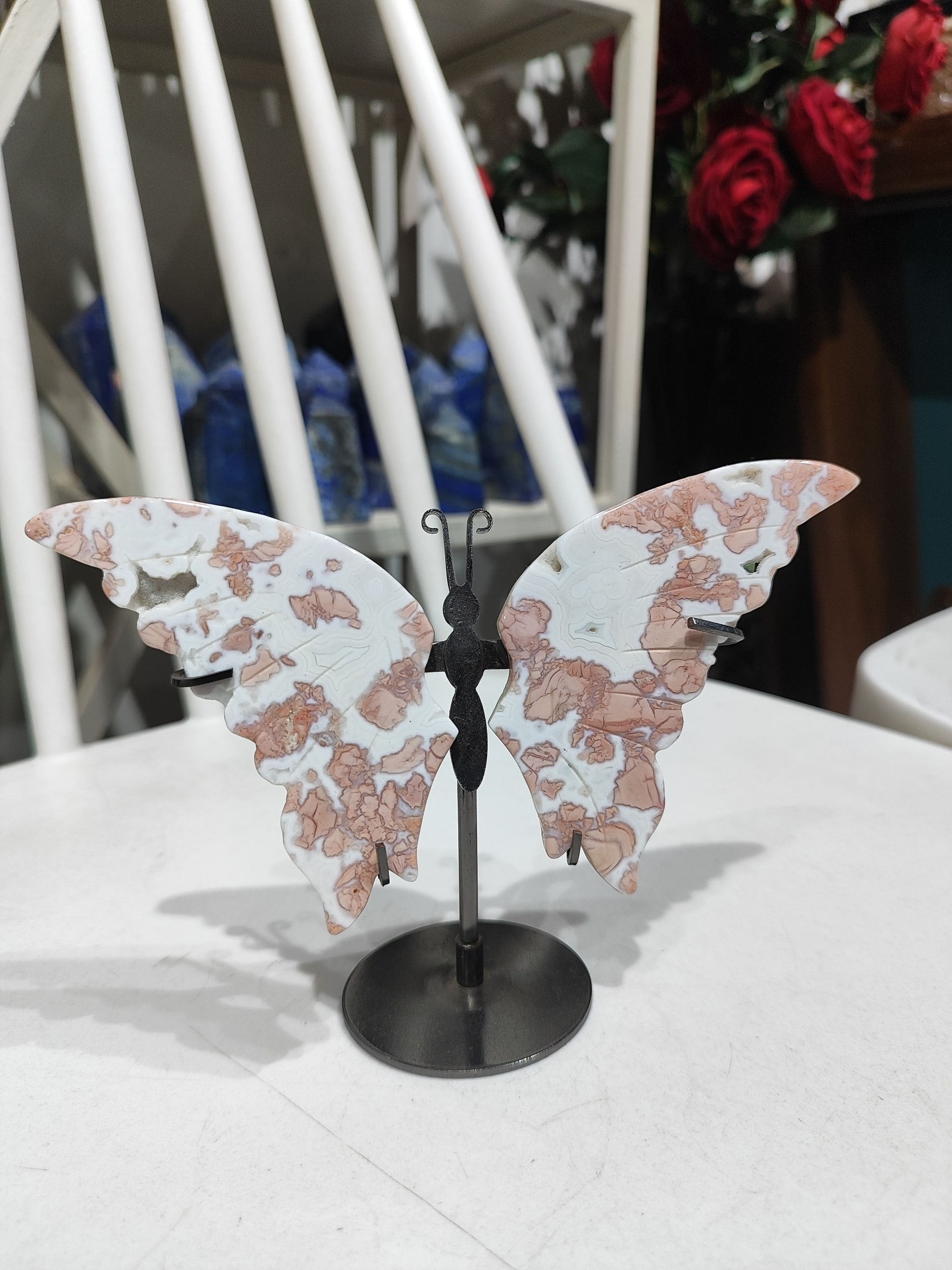 A carved Pink Amethyst crystal shaped like a butterfly with intricate pink and white patterns, mounted on a sleek black me — MB Global Agate